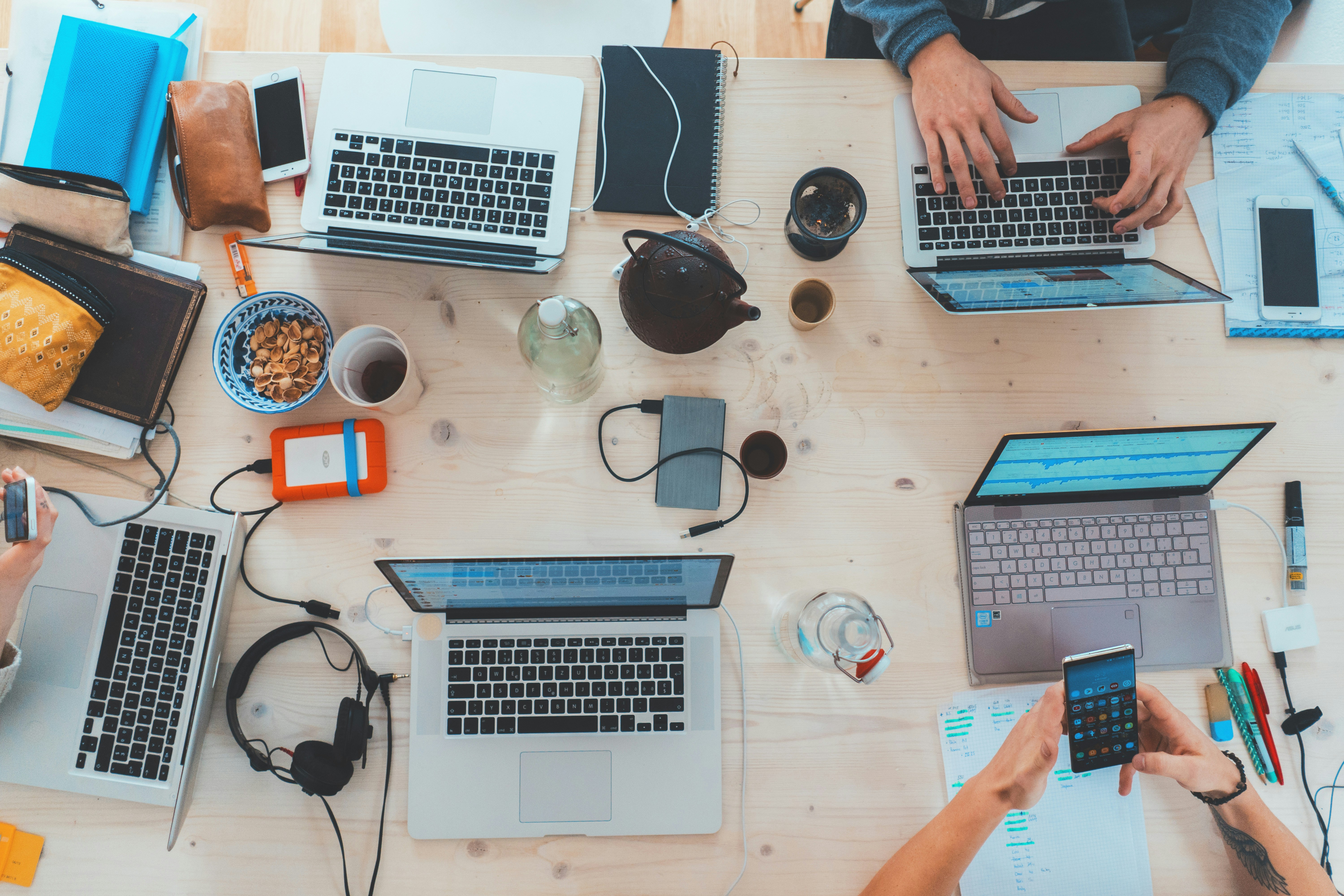 Overhead workspace with laptops, phones, notebooks, and project planning materials.