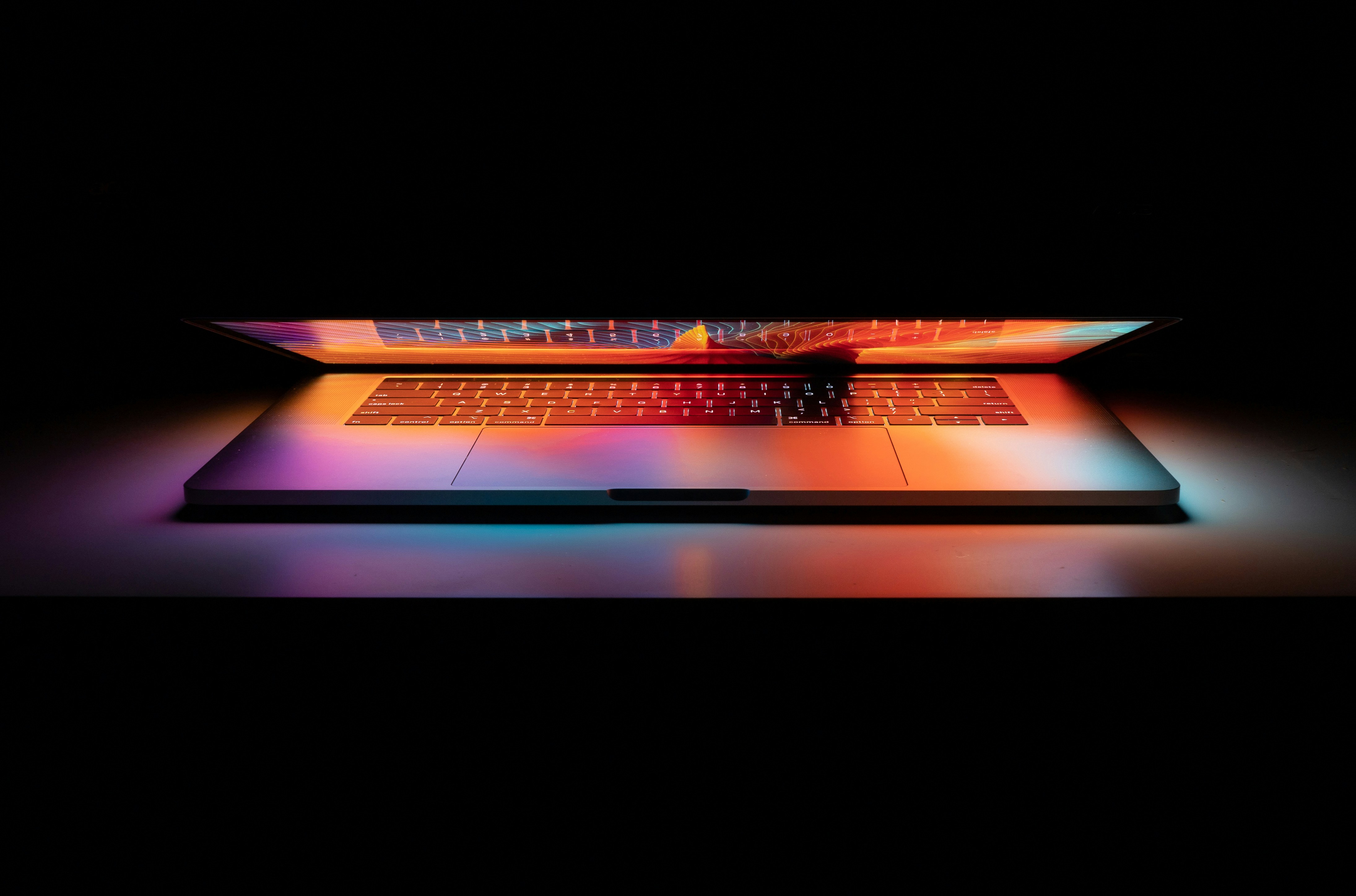 Open laptop glowing with colorful light against a dark background.